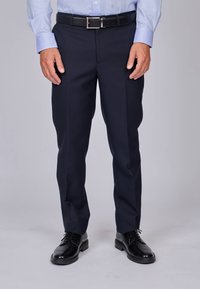 Pantalons de costume navy en tissu lisse, avec une coupe ajustée et des jambes droites ; portés avec une ceinture en cuir noir et des chaussures de ville noires.