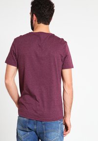Bordeauxrotes Kurzarm-T-Shirt aus weichem Material, mit Rundhalsausschnitt und lockerer Passform. Getragen mit blauen Jeans, die einen lässigen Stil unterstreichen.