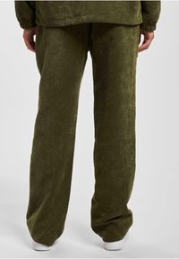 Pantalones de pana verde oliva con una superficie texturizada de costillas, diseño de pierna ancha y un ajuste relajado, que llevan zapatillas blancas abajo.