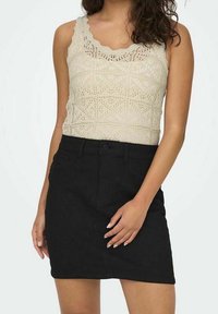 Top de tirantes beige de crochet con bordes en forma de conchas combinado con una minifalda de mezclilla negra que presenta bolsillos delanteros y un diseño ajustado.