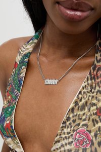Collana in argento con pendente metallico che riporta la scritta "EDWARDY", caratterizzato da un design frastagliato. Indossato sopra un top in tessuto fantasia.