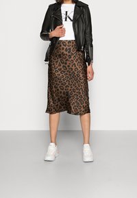 Brun leopardmönstrad midikjol ihop med en svart läderjacka och vita sneakers. Kjolen har en mjuk textur och en svävande silhuett.