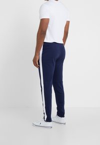 Navy joggers med vita sidostråk, elastisk midja, tapered fit, kombinerat med en enkel vit t-shirt och vita sneakers.