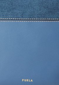 Blue leather wallet with a textured denim accent, featuring white stitching and a gold "FURLA" logo at the bottom.