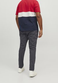 Kortärmad T-shirt med röda, vita och marinblå horisontella ränder, kombinerad med mörkgrå byxor och vita skor, sedd från baksidan.