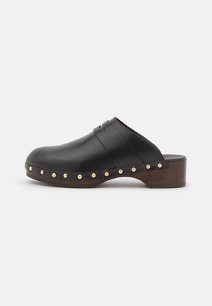 Zueco negro de cuero sin cordones con suela de madera y tacón bajo, decorado con tachuelas de tono dorado a lo largo del borde.