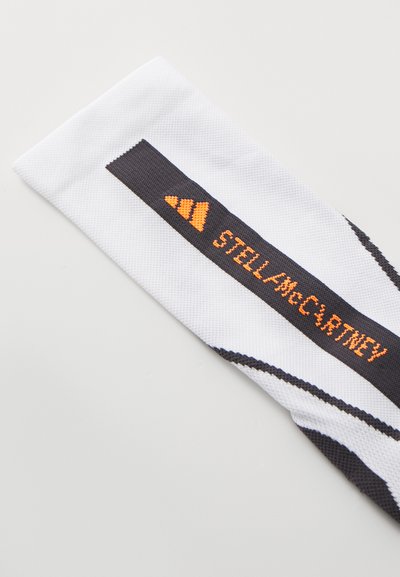 White sports headband with black and orange "STELLA McCARTNEY" text. Features diagonal black stripes and a textured fabric.