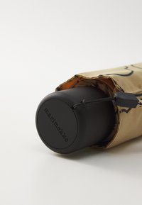 Conteneur cylindrique noir partiellement recouvert d'une manche en tissu doré avec un motif imprimé noir. Le conteneur possède un logo et un cordon ajustable.
