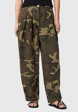 Løse camouflagebukser med plisseringer båret med sorte sandaler, der viser modellens ben fra talje til fødder.