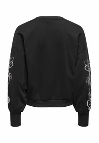 Melnā džemperī ar balonu piedurknēm, ribotiem aproces galiem, īsā dizainā un gaiši pelēku ziedu izšuvumu uz piedurknēm. Gluda auduma tekstūra.