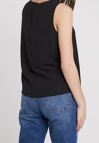 Svart ärmlös topp med en mjuk textur och en subtil söm på baksidan, parat med högmidjade blå denimjeans med bakfickor.