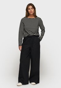 Gestreepte langemouwenshirt in zwart en crème, gecombineerd met hoge taille, wijde zwarte broek. Soepele stof met een ontspannen pasvorm.