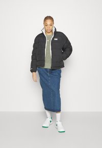 Black puffer jacket with a quilted design and gray trim, layered over a green sweater and paired with a denim skirt and white sneakers.
