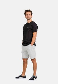 Camiseta de algodón negra, pantalones cortos grises claros y zapatillas negras. La camiseta tiene un pequeño logotipo en el pecho. Los pantalones cortos cuentan con bolsillos delanteros.