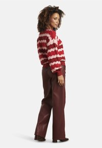 Red and pink zigzag-patterned sweater with ribbed cuffs and hem; paired with high-waisted, glossy burgundy faux leather pants and heeled shoes.