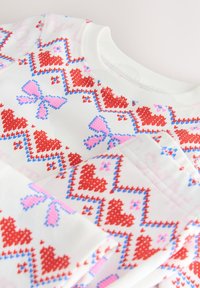 White sweatshirt featuring a knit pattern with red hearts and pink bows, accentuated by blue outlines and a soft texture.