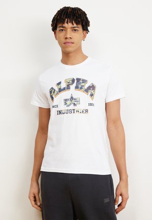 Camiseta blanca de algodón con un logotipo gráfico multicolor "ALPHA INDUSTRIES" en el frente, con mangas cortas y un escote redondo.