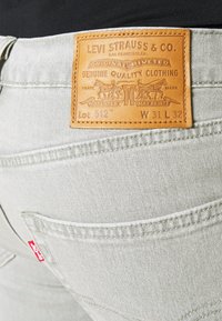 Ljusgrå jeans med en läderlapp med präglad logotyp. Lappen visar "Levi Strauss & Co." och skötselråd.