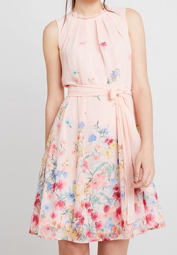 Ein ärmelloses pinkes Kleid mit einem gefältelten Ausschnitt, das ein florales Muster in verschiedenen Farben und einen gebundenen Gürtel in der Taille aufweist.
