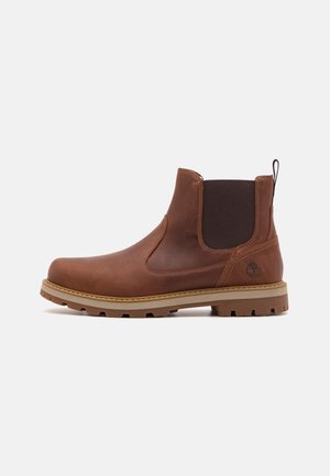 Brązowy skórzany botek za kostkę z elastycznym bocznym panelem, pętelką na pięcie oraz beżową, gumową podeszwą z agresywnym bieżnikiem. Wytłoczone logo Timberland w pobliżu pięty.