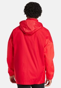 Rode waterdichte jas met capuchon, lange mouwen, elastische manchetten en een relaxte pasvorm. Glad textuur, minimale details en effen kleur.