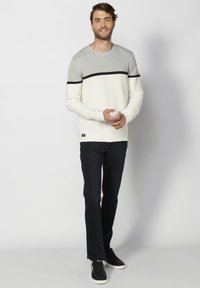 Pullover a maniche lunghe grigio e bianco con righe orizzontali, caratterizzato da un collo rotondo, una texture a coste e un piccolo patch con logo sull'orlo.