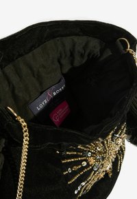 Interiér kabelky z čierneho zamatového materiálu s retiazkou v zlatej farbe, ozdobnými korálkami a štítkami značky. Mäkká textúra so štruktúrovaným tvarom.