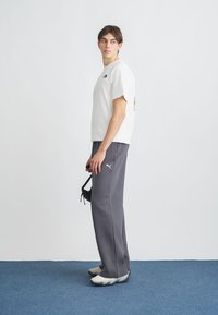 Λευκό κοντομάνικο μπλουζάκι με λογότυπο, σε συνδυασμό με γκρι φόρμα και γκρι αθλητικά παπούτσια. Το σύνολο έχει casual σχεδιασμό και άνετη εφαρμογή.