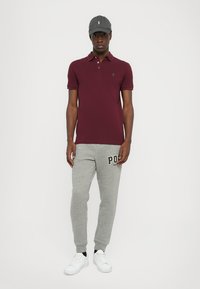 Burgundska polo majica, sivi trenirci s printom "Polo", siva kapa i bijele tenisice. Jednostavan dizajn, pamučni materijal, ležeran kroj.