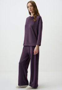 Ensemble composé d'un haut à manches longues violet et d'un pantalon large, fabriqué en tissu doux. Présente une coupe décontractée, un col rond et une texture subtile.