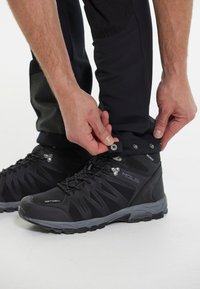 Bottes extérieures noires imperméables avec une semelle robuste, fabriquées en matériau souple, équipées de manchons de cheville ajustables et de coques de protection renforcées.