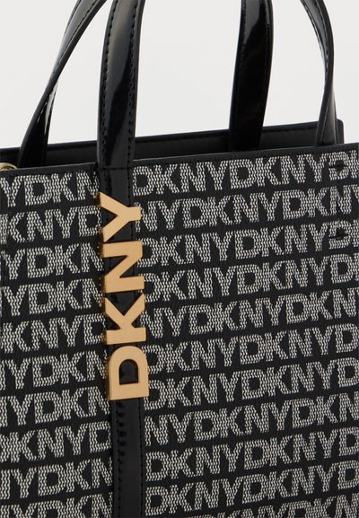Sac cabas DKNY à motifs noirs et blancs avec poignées noires brillantes et logo vertical doré "DKNY" sur le devant.