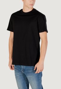 Must mustern jahe T-särk lühikeste varrukatega, ümar kaelus ja mugav lõige, ühendatud heledate siniste teksadega.