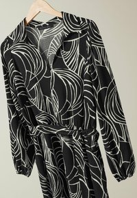 Zwarte jurk met een wit bladmotief, met een kraaghalslijn, lange mouwen, een taille met riem en een gestructureerde stof.
