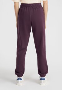 Paarse sweatpants met elastische tailleband en boorden, gemaakt van zachte stof. Draagt met witte sneakers met blauwe accenten.