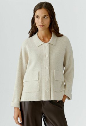 Lichtbeige cardigan met een met kraag afgewerkte halslijn, knopen aan de voorkant en twee voorzakken. De stof heeft een zachte, gestructureerde uitstraling.
