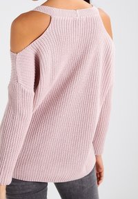 Pull rose en tricot avec découpes aux épaules, texture côtelée et coupe décontractée. Manches longues avec épaules tombantes.