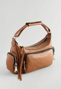 Sac à main en cuir marron avec trois compartiments zippés, poignée doublement cousue et tirettes de fermeture éclair en métal argenté sur un fond neutre.