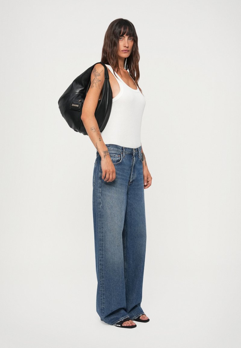 Wide-leg denim jeans in light blue, paired with a white tank top. The model carries a black bag with a smooth texture and gold hardware.