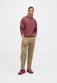 Sweatshirt bordeaux avec col rond et broderie, pantalon en velours côtelé beige, et chaussures de sport roses vives avec des accents noirs.