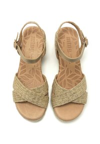 Sandales tissées beiges avec un design à brides croisées, une sangle de cheville ajustable et une semelle texturée ornée de motifs de feuilles. Style à bout ouvert.