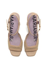Sandalias de tacón abiertas de color beige con un acento trenzado, correa ajustable en el tobillo y una plantilla acolchada color lila que presenta el nombre de la marca "MARIAMARE."