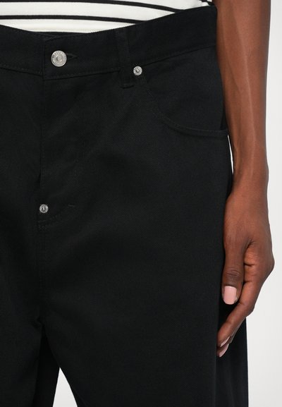 Schwarze Jeans aus Denim mit einem figurbetonten Design, ausgestattet mit silbernen Beschlägen, fünf Taschen und einer strukturierten Oberfläche. Der Bund ist leicht erhöht.