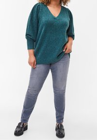 Dzianinowy sweter w kolorze morskim z dekoltem w serek, oversize'owymi rękawami i luźnym krojem, zestawiony z szarymi obcisłymi jeansami i czarnymi loafersami na platformie.