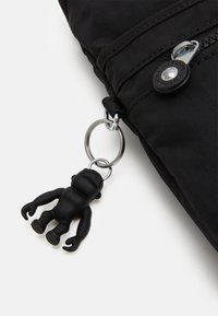 Borsa di stoffa nera con chiusura a zip, un bottone rotondo e un portachiavi a forma di scimmia in gomma attaccato tramite un anello metallico.