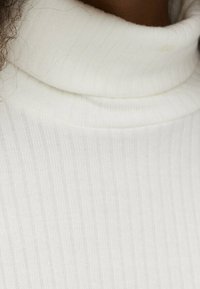 Maglione bianco a collo alto a costine caratterizzato da una texture morbida e una vestibilità aderente. Il tessuto presenta righe verticali, che aggiungono un tocco raffinato al design.