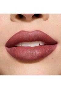 Labial mate en un tono malva oscuro sobre labios llenos, mostrando un acabado liso y texturizado con un brillo sutil bajo la luz natural.