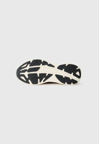 Sorte og kremfargede gummisåler til sneakers med en teksturert overflate og et distinkt dekkmønster for traction og fleksibilitet.
