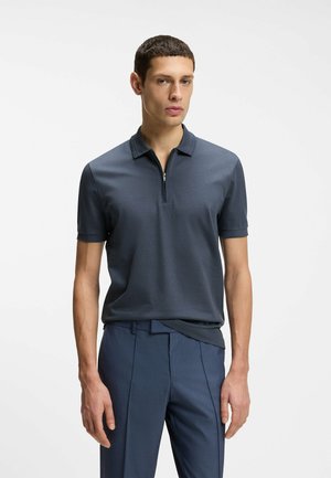 Kurzärmeliges Poloshirt in Dunkelgrau mit einem Reißverschluss am Kragen und einem strukturierten Stoff, kombiniert mit enganliegenden marineblauen Hosen.