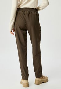 Dunkelbraune Jogginghose mit elastischem Bund und Seitentaschen, aus leichtem Stoff. Modell trägt beige Schuhe.